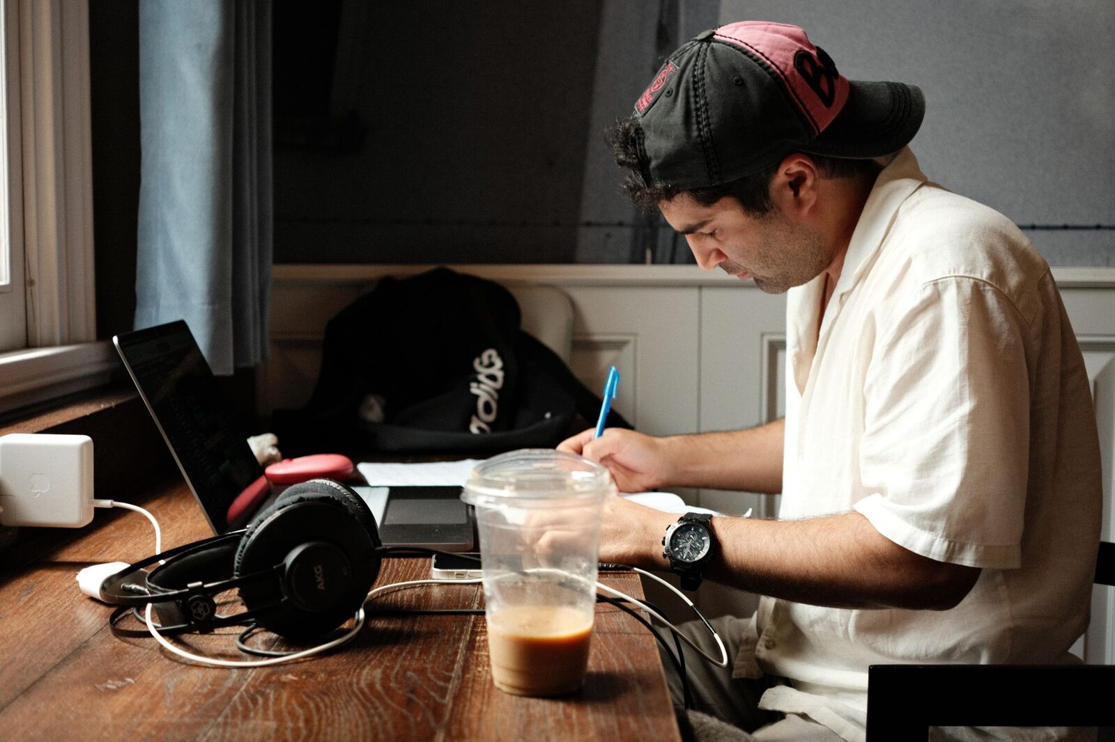 Focused man writing at a desk with coffee, laptop, and headphones nearby.